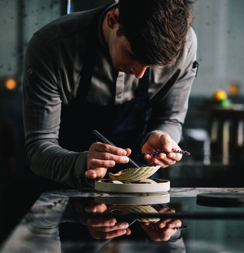 chef Filip Hanlo preparing a clam dish in its shell at chef's table restaurant até amsterdam