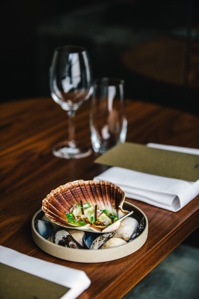 A clam dish served at the table at até amsterdam, next to a wine glass and napkin
