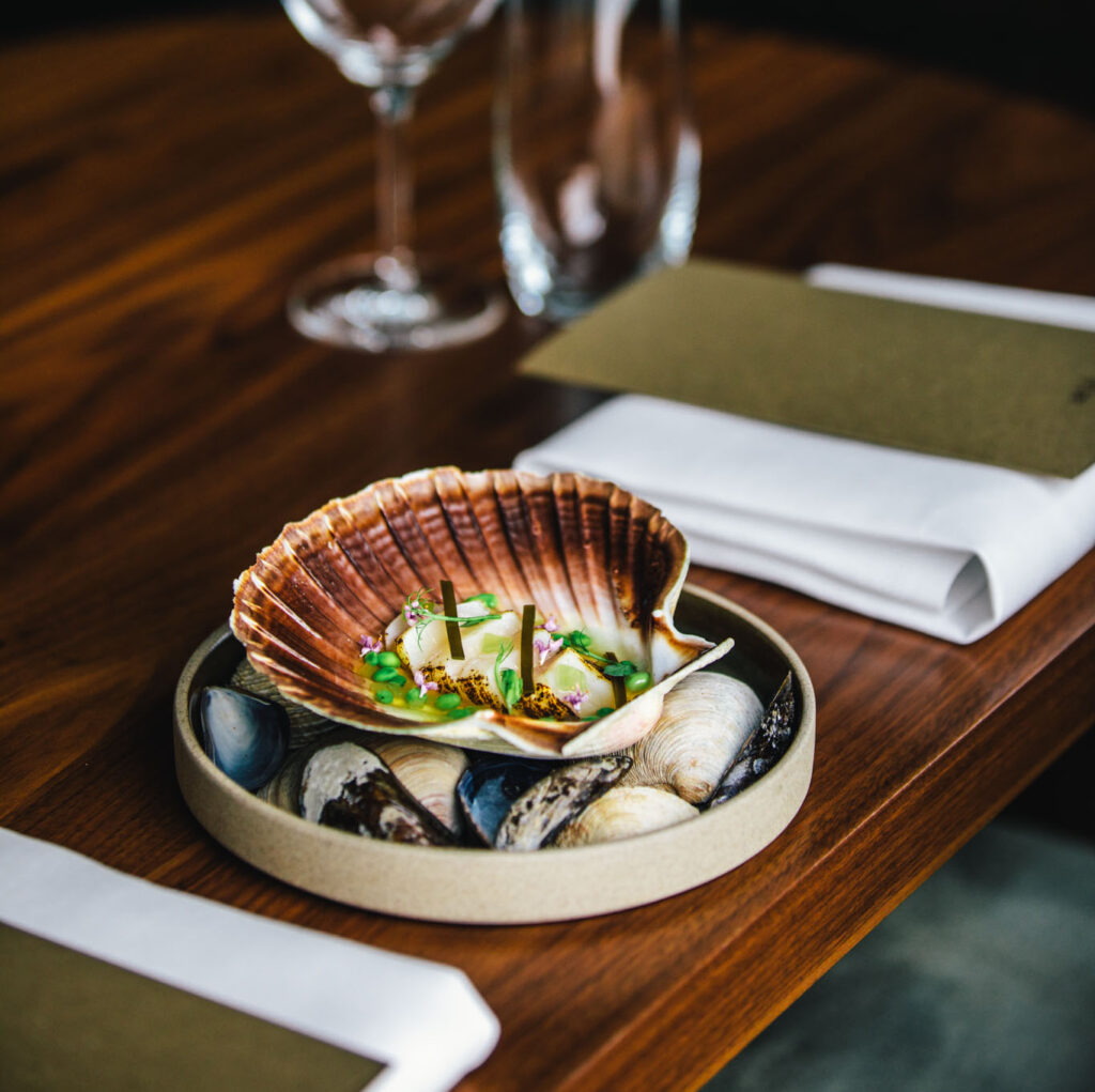 A clam dish served at the table at até amsterdam, next to a wine glass and napkin